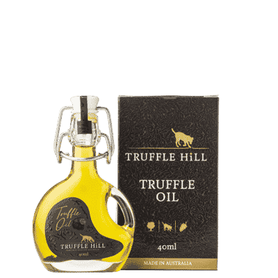 A small pourer style bottle of golden truffle oil with a black labell placed in front of a black box with Truffle Hill branding.