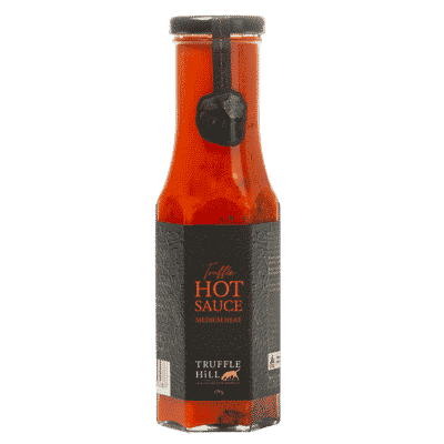 A hexagonal sauce bottle filled with red chilli sauce with a black Truffle Hill label.